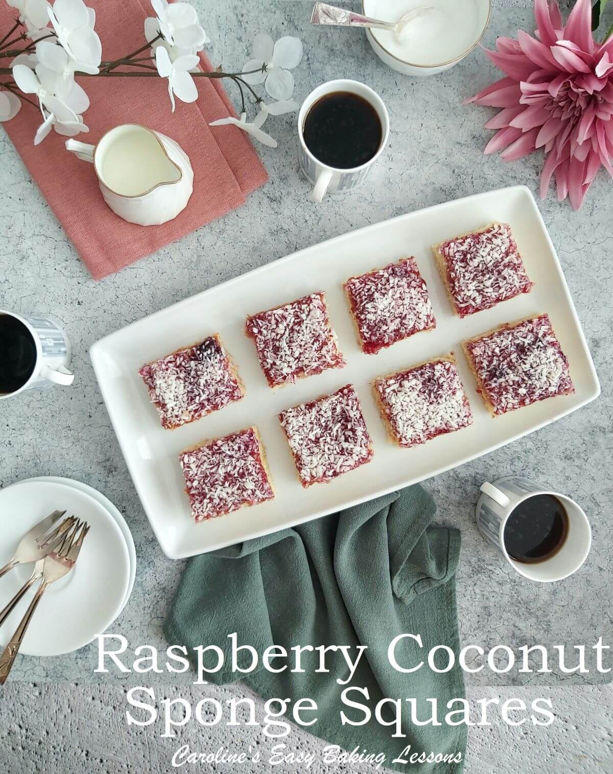 Raspberry coconut sponge squares on a white plater on a dinner table.