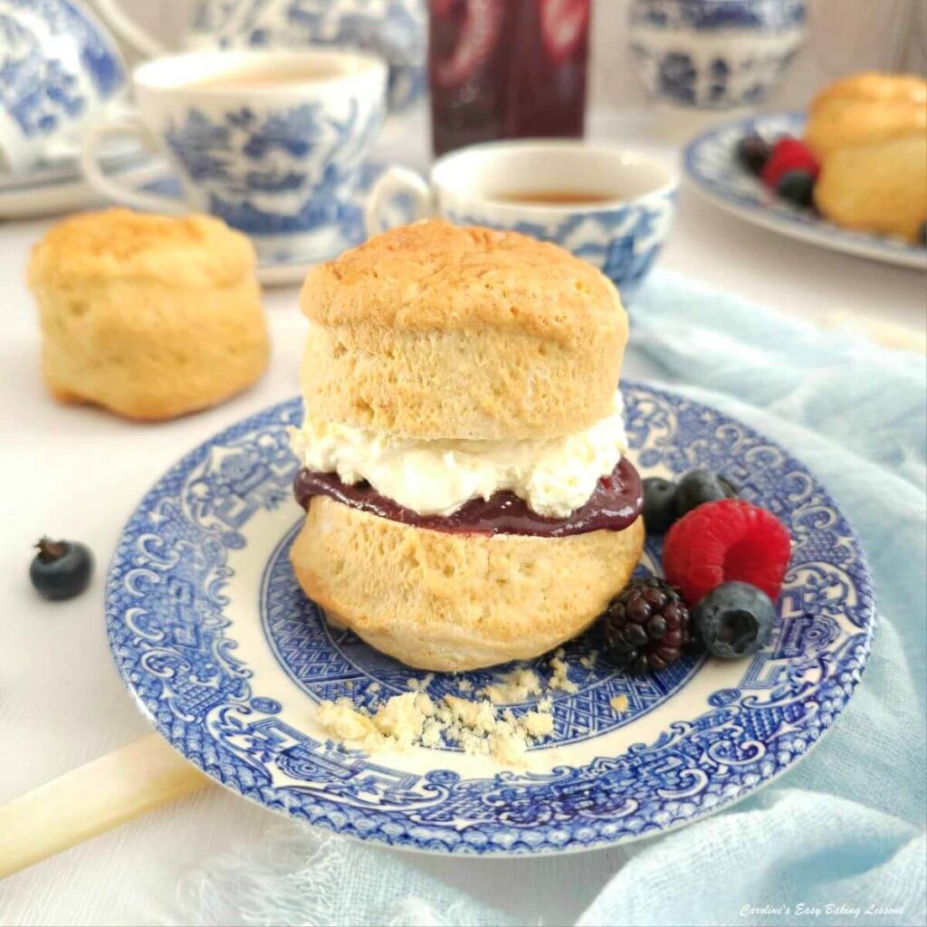 Close front shot of a tall jam and cream filled British scone, served on blue & white vintage crockery.