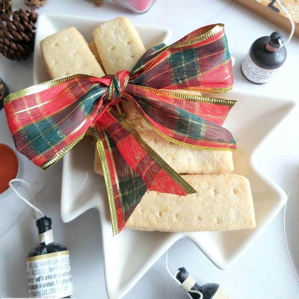 Close overhead shot of Christmas tree shape white plate, with Scottish shortbread finger biscuits/cookies on top with party poppers to the side.