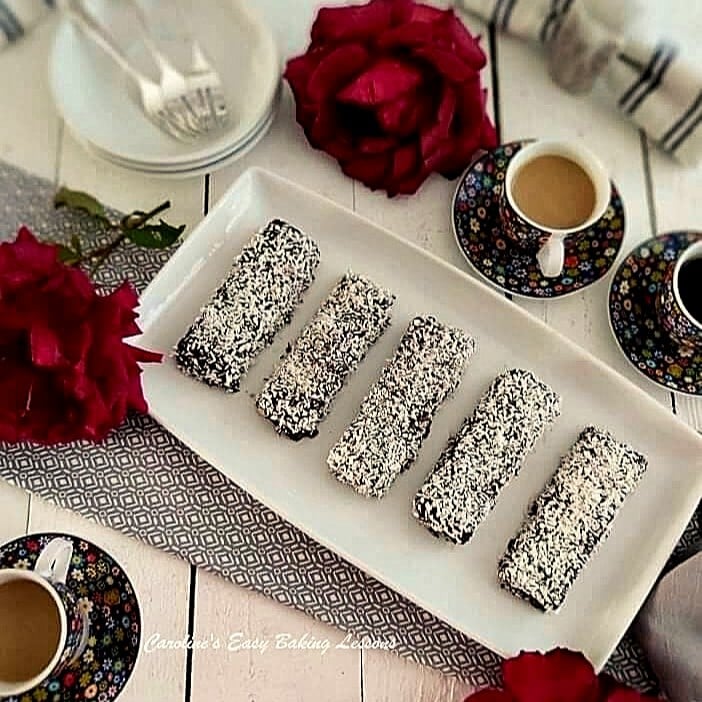 Overhead photo of white table with tea large roses, teacups, surrounding coconut and chocolate long Lamington cakes.