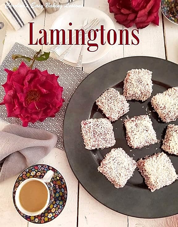 Overhead shot of white table top with large red roses, tea cups, and round plate of raspberry jam coconut square cakes, with text 'Lamingtons'.