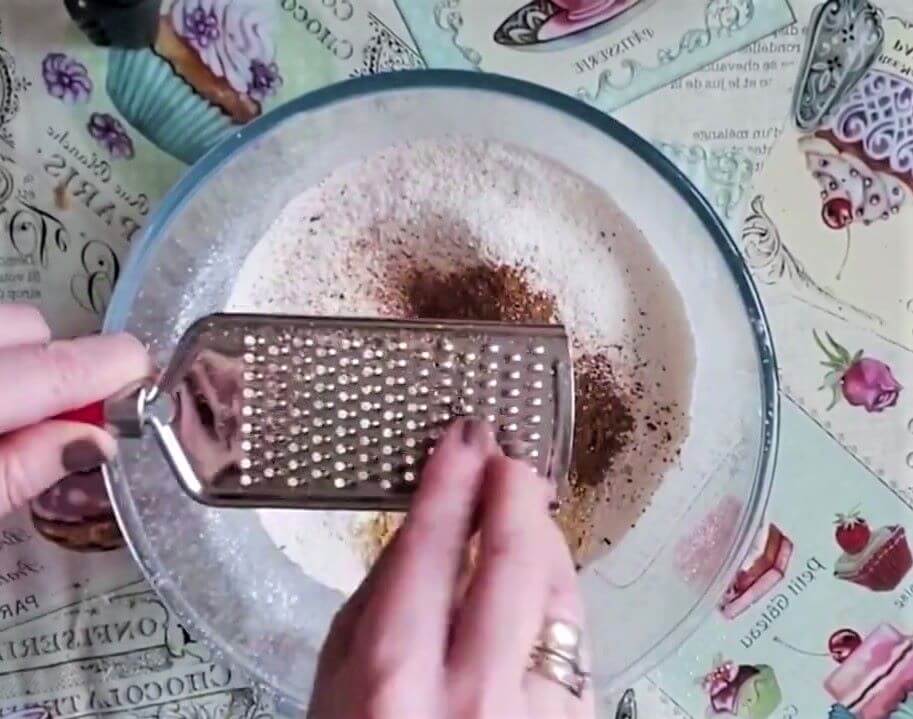 Grating fresh nutmeg into the bowl of dry ingredients.