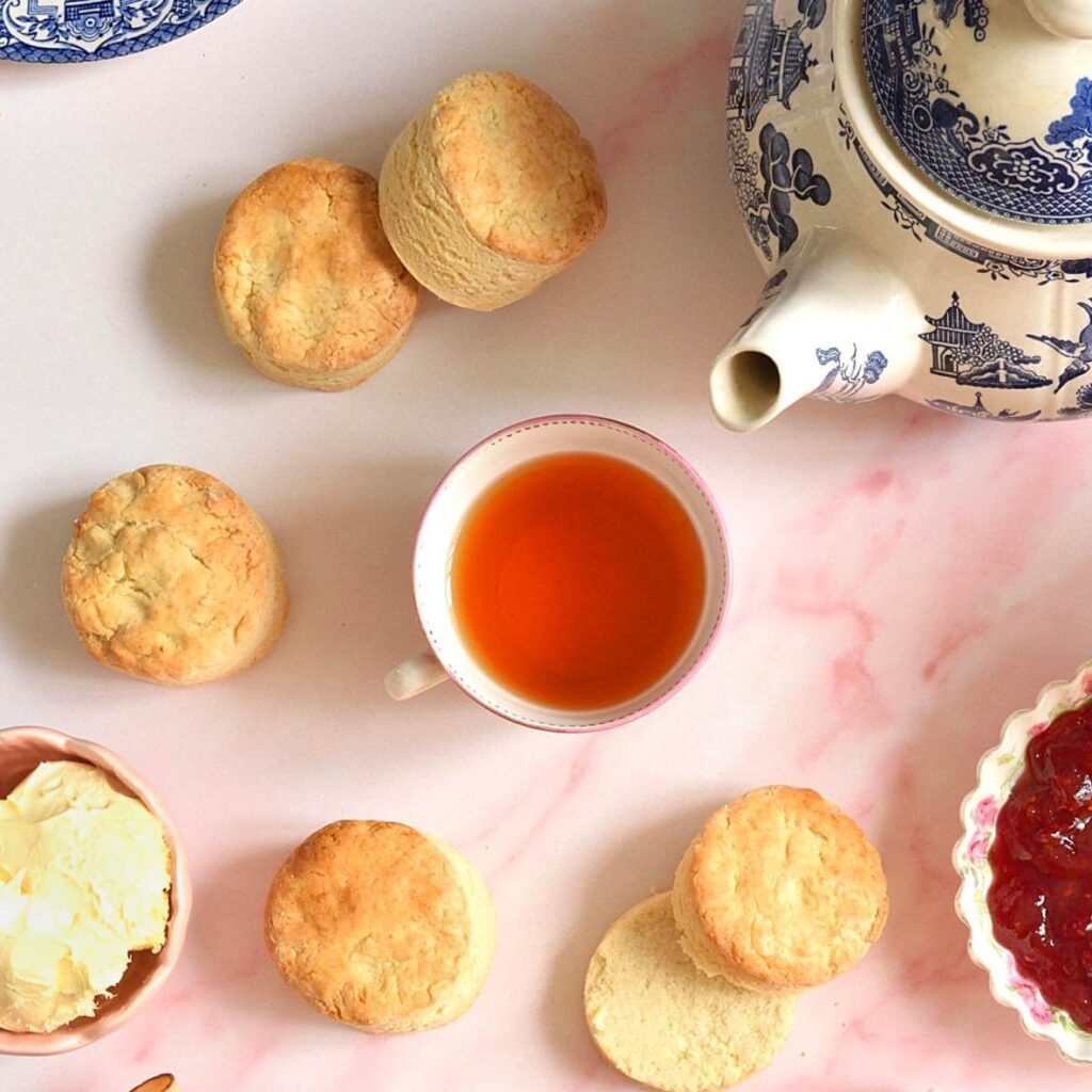 Close overhead cropped shot of white pink marbletable, with teapot and British scones, clotted cream and jam bowls & tea in the centre.