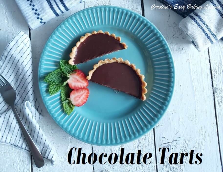 Individual chocolate tart cut in half on a blue plate served with a strawberry.