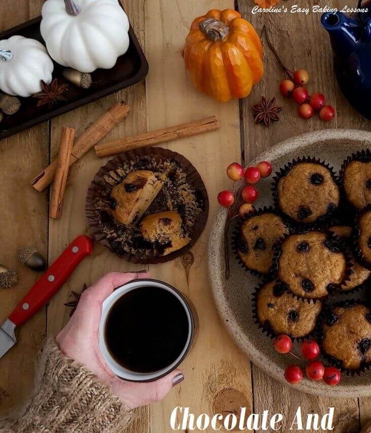 Hand around mug of hot coffee & chocolate spotted pumpkin muffins, around AUtumn decorations.