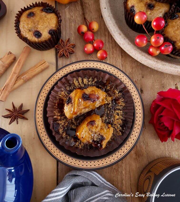 Overheat flatlay pic of a wooden table with chocolate pumpkin muffins and cinnamon sticks and one served with syrup.