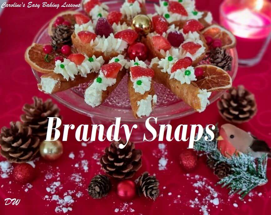 front on shot of glass plate of brandy snap tubes wth cream and strawberries pieces with Christmas candle to the side & title brandy snaps.
