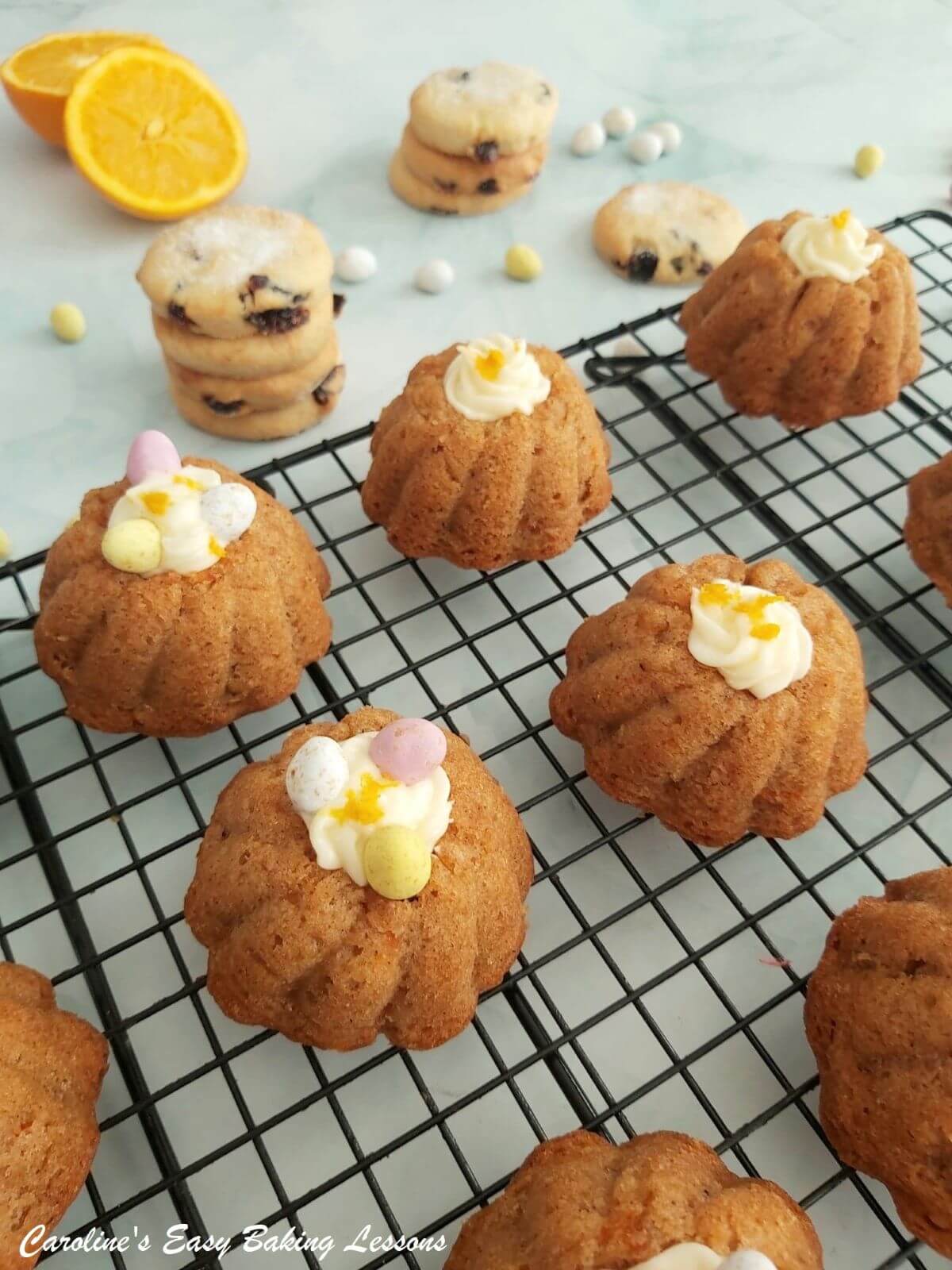 Closer shot of mini carrot bundt cakes with cream cheese frosting orange zest and some mini eggs, on a cooling rack.