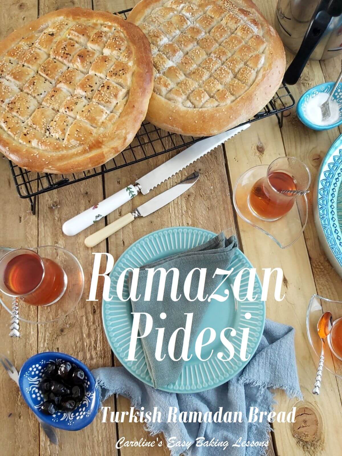 Overhead wooden table shot of ramazan round thick flatbread with diamond pattern, cooling next to Turkish tea and plates with title.