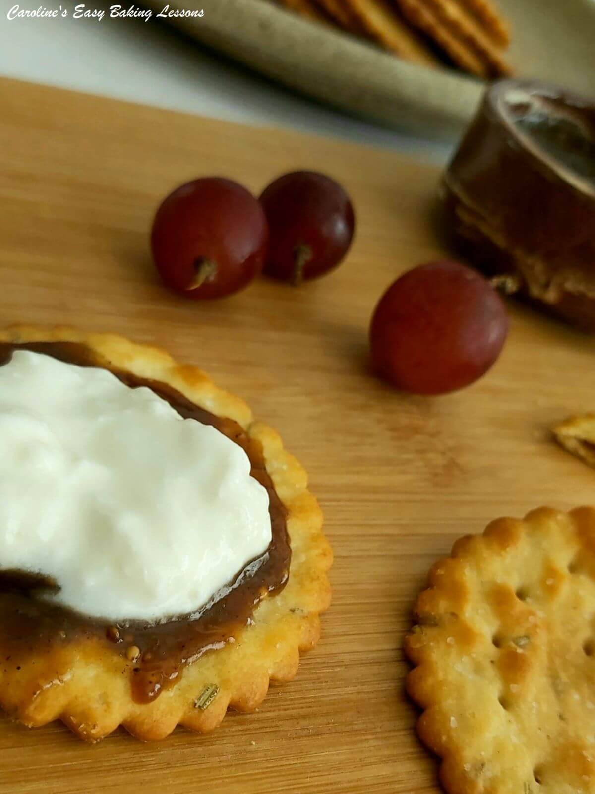 Extra close show of a golden round herb studded cracker with brown fig curd and cottage cheese with red grapes to the background.