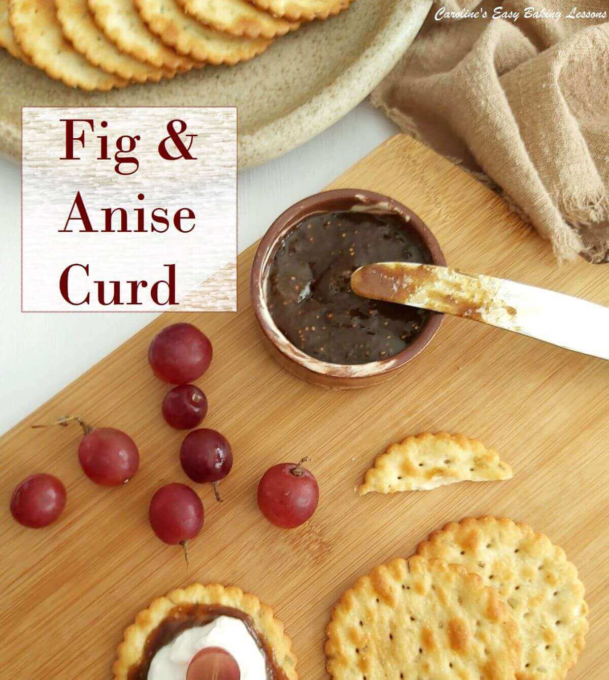 Overhead of wooden chopping board, crackers, red grapes, brown fig curd and on crackers and white cheese with fig anise curd title.