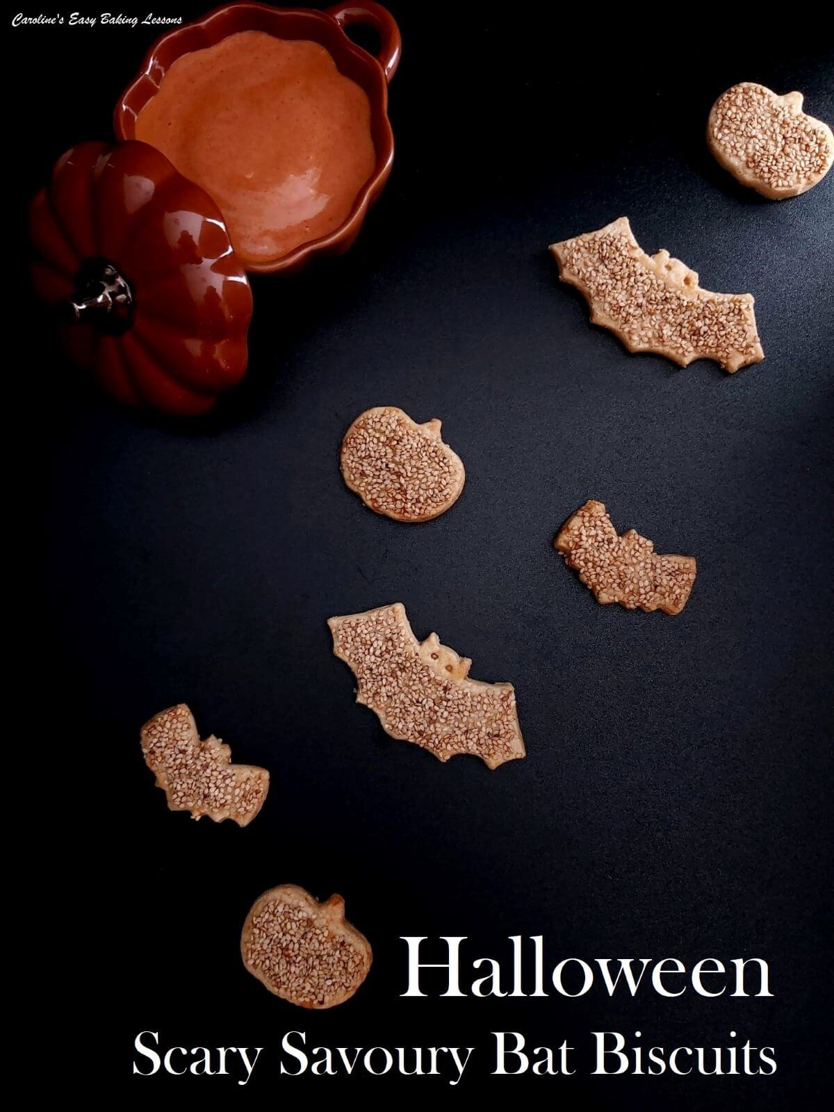 Overhead of savoury bat cookies appearing to fly, on a black backdrop, with light shinning through one corner, with a brown pumpkin dish and dip to the side.