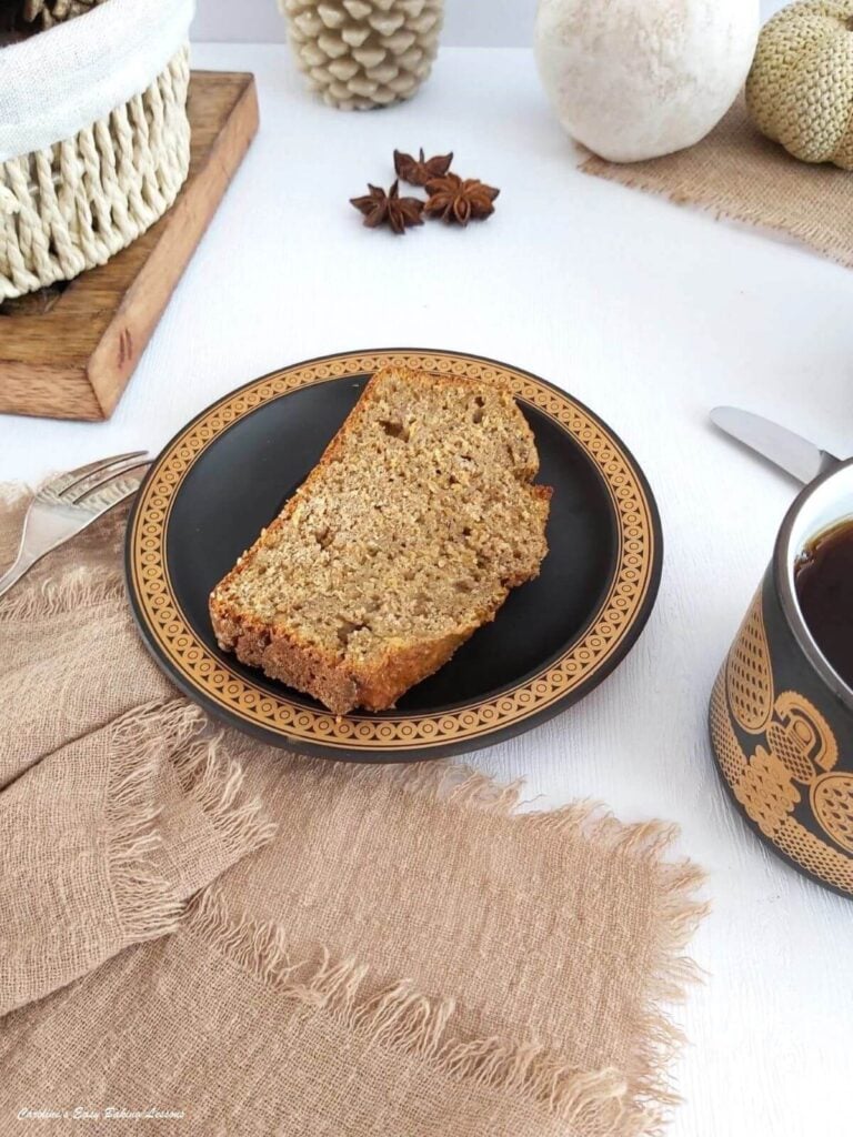 Slice of wholemeal squash banana bread ona plate with coffee to the side.