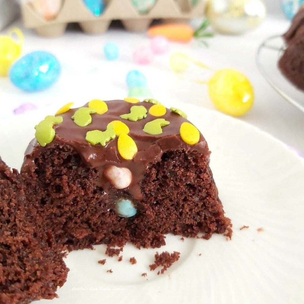 Extra close shot of a halved mini chocolate bundt cake, with Easter sprinkles on top of chocolateganache, and tiny pastel coloured mini eggs inside.