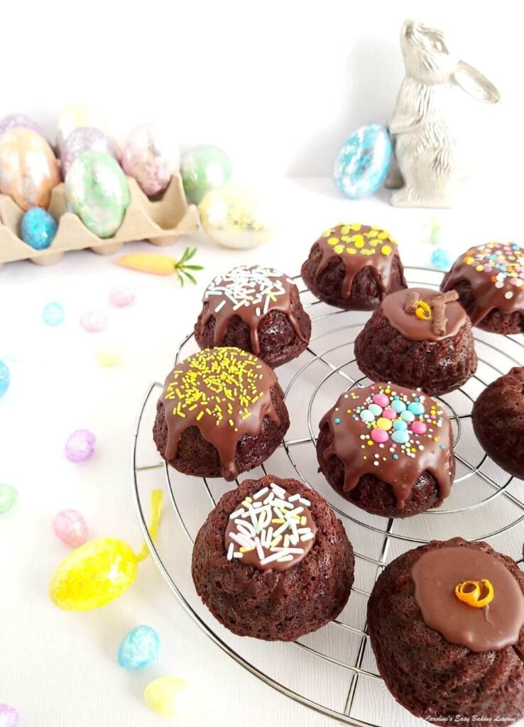 Overhead shot of mini chocolate bundt cakes decorated, on a wire rack and Easter eggsdecoration around.