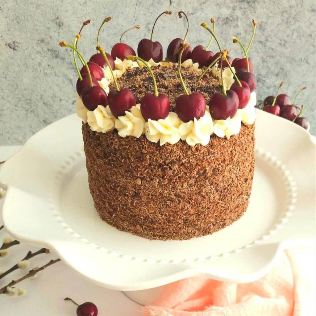 Close shot of a tall 6 inch air fryer Black Forest Gateau cake with chocolate coated sides, and cream and cherry topped decoration.