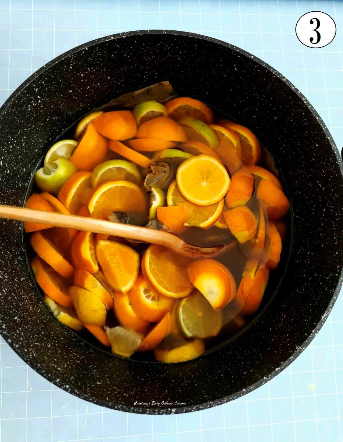 Overhead close shot of large black cooking pot full of slices of lemons, oranges and limes in water - photo 3.