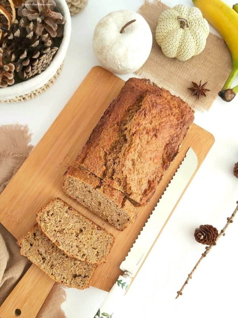 Overhead shot of brown load on chopping board,with sloces cut, banana and Autumn decorations to the sides.