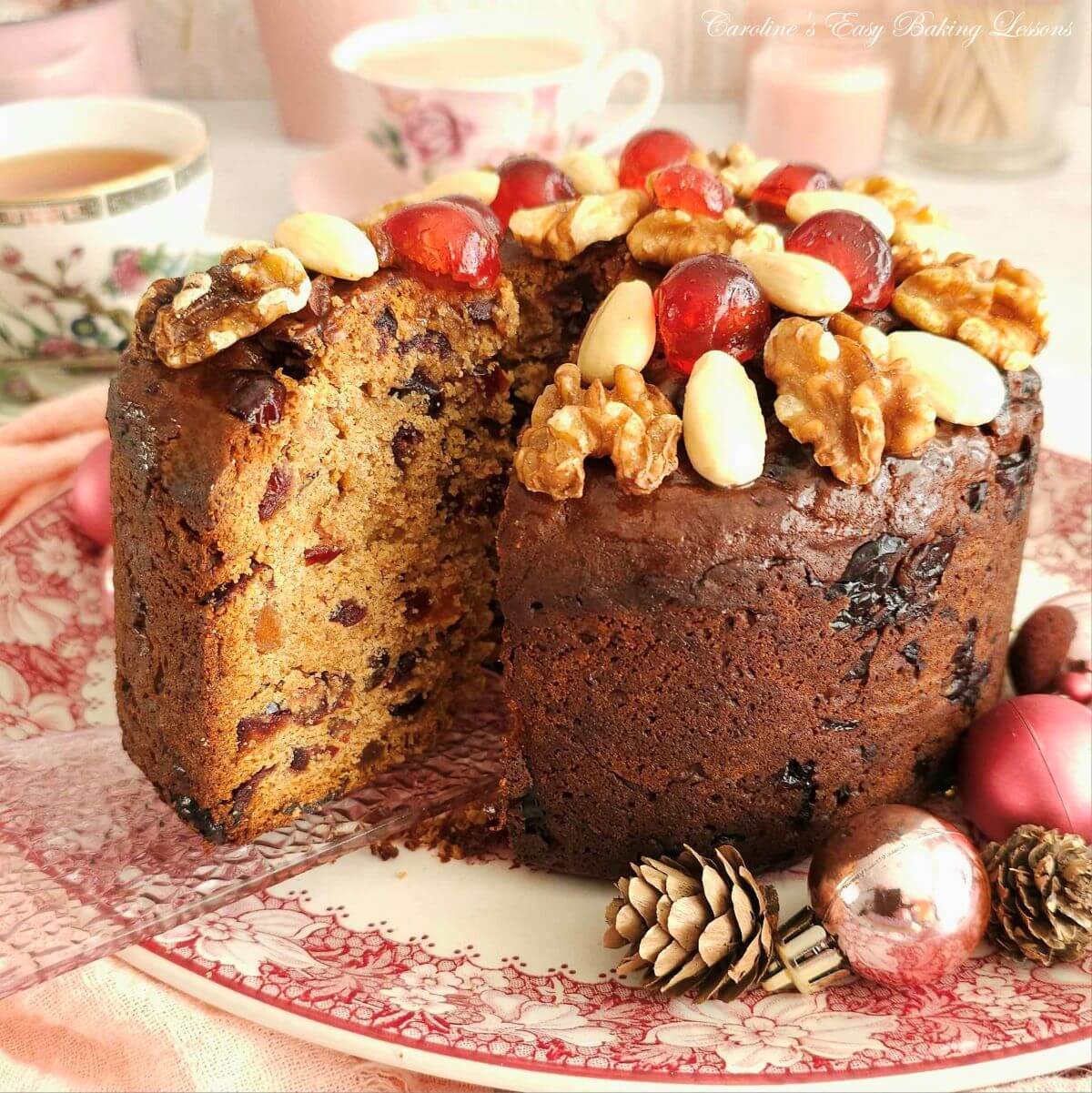 Close square shot of a nut and cherry topped fruit cake with slice about to be removed.