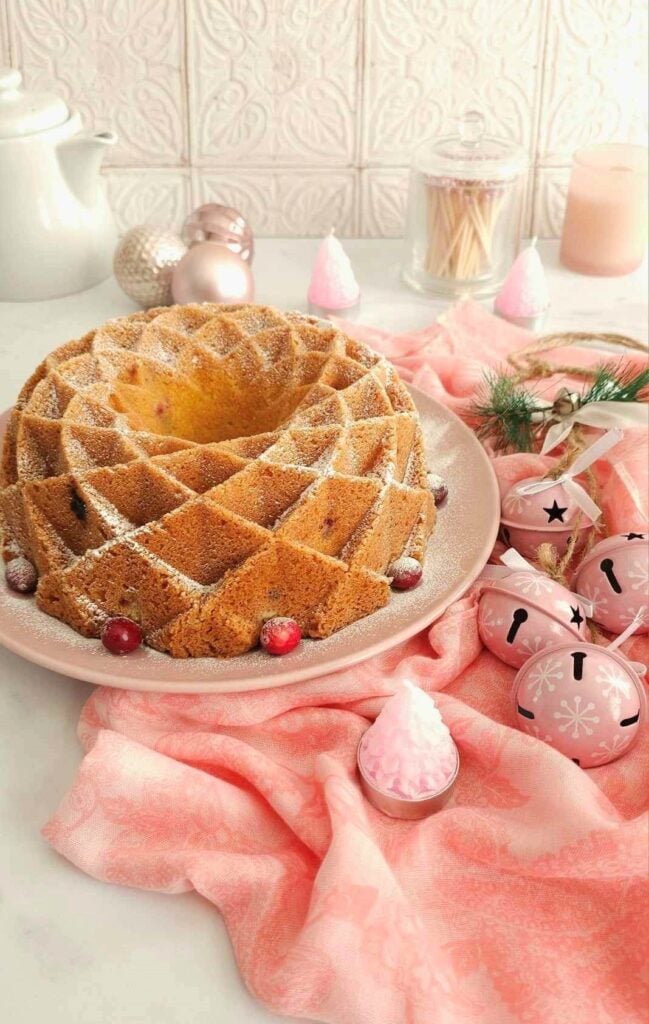 Long shot of a pink Christmas decorated table with pink napkin and a intricate detailed cranberry orange bundt cake.