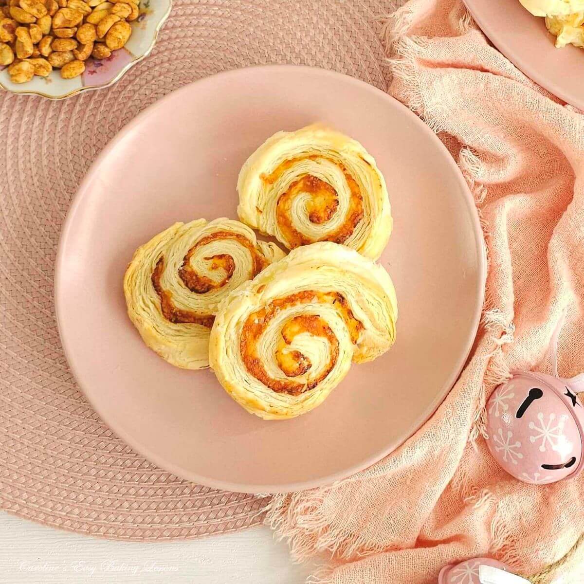 Overhead close shot of table with pink plate and napkin, with nuts tot eh site and 3 cheese spiral pastries served.