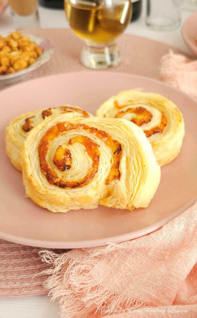 Extra close shot of 3 cheese pastry swirls on a pink plate, showing the layters of puff pastry.