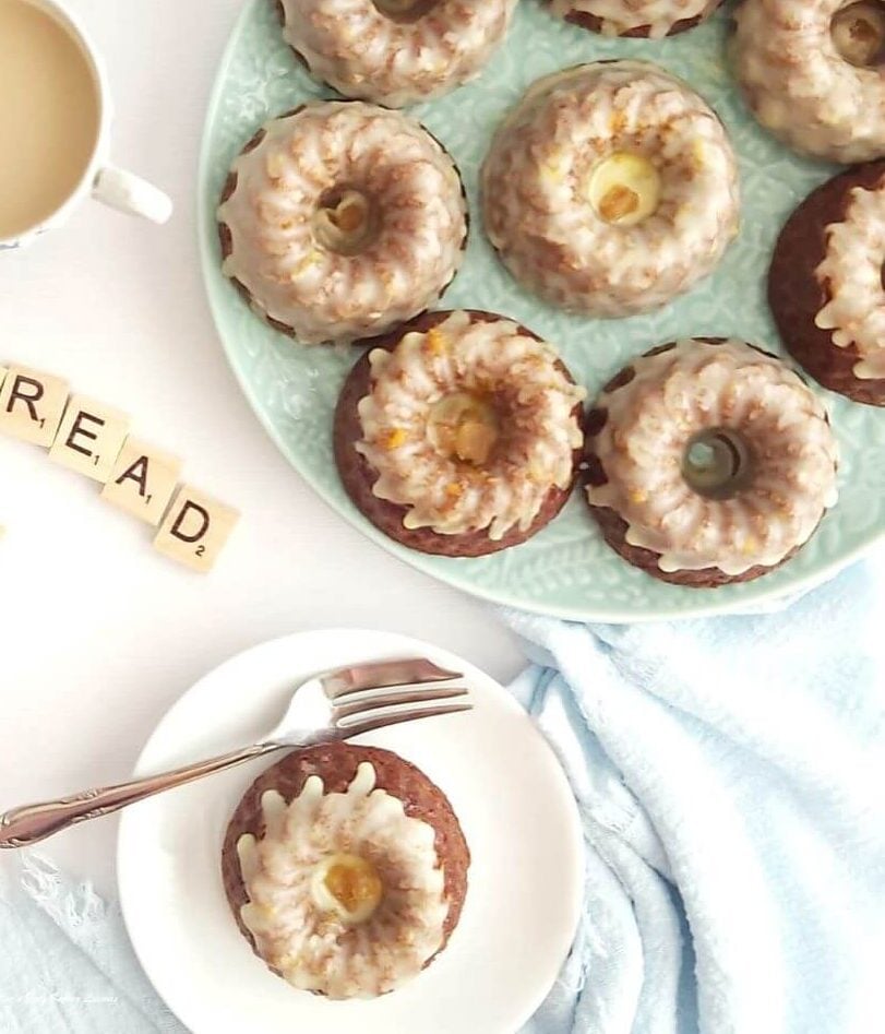 Overhead photo of white table and green plate of several glazed mini bundt cakes, and one served with partial text showing'bread' for gingerbread cake.