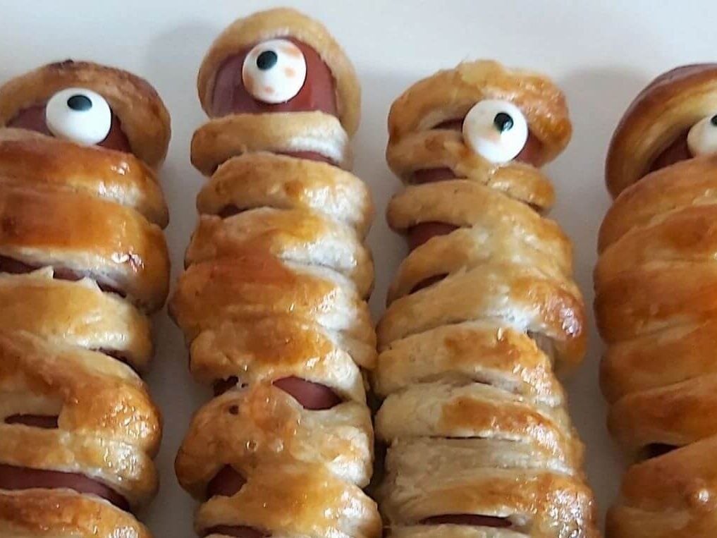 Cloase photo of 4 scray one eyed mummies by kids, made from sausage rolls and puff pastry and candy eye.