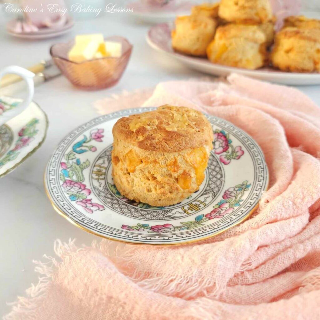 Extra Close shot of tall British cheese scone on pink vintage plate, with more to the background, pink napkin and butter dish to the background.