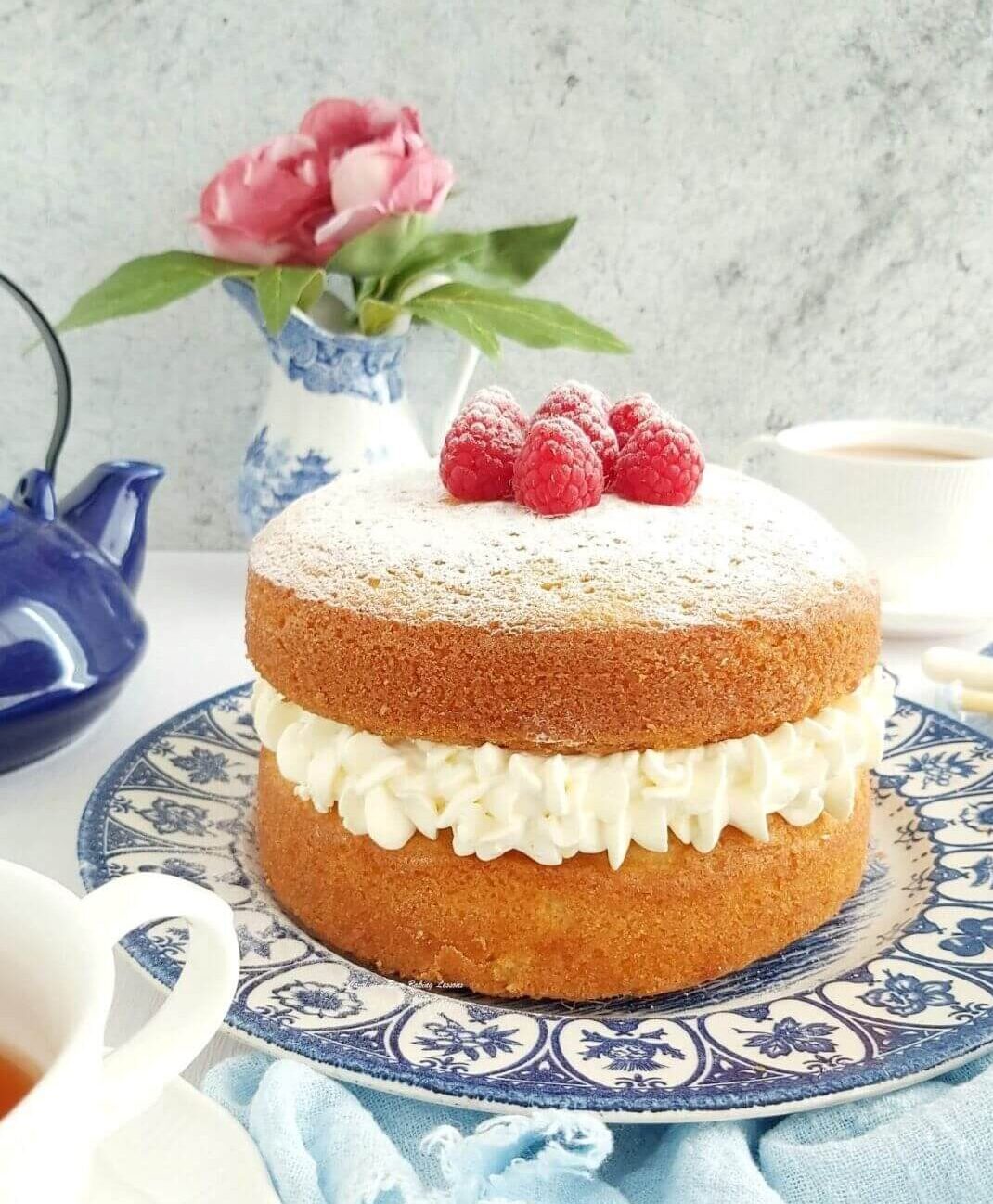 Cream filled layer cake on table with teapot and cup to the side.