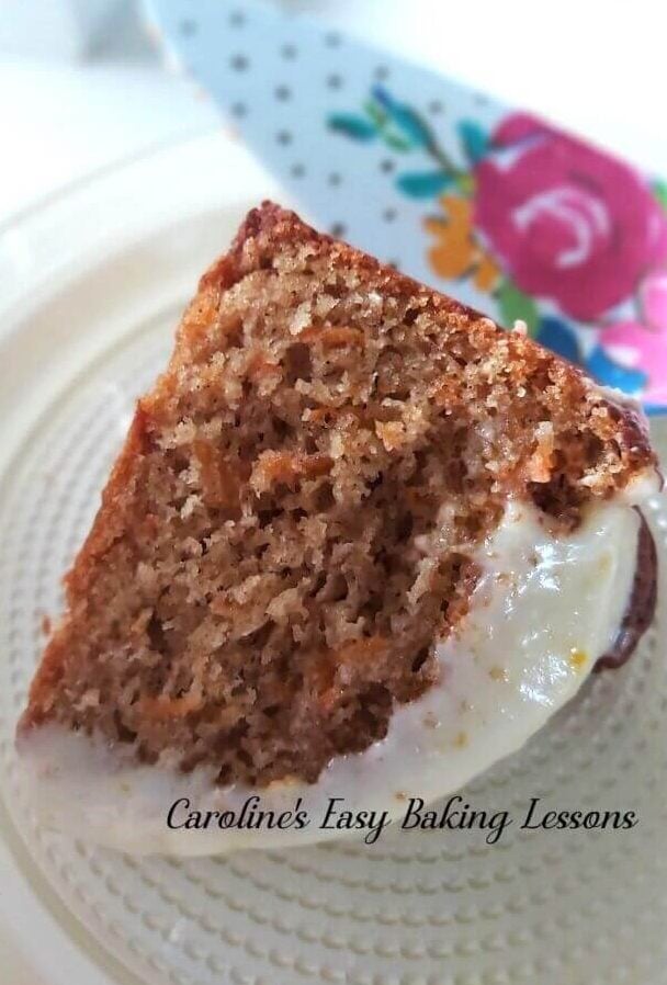 Side shot of a slice of gluten free carrot bundt cake with cream cheese frosting, served on a white plate.