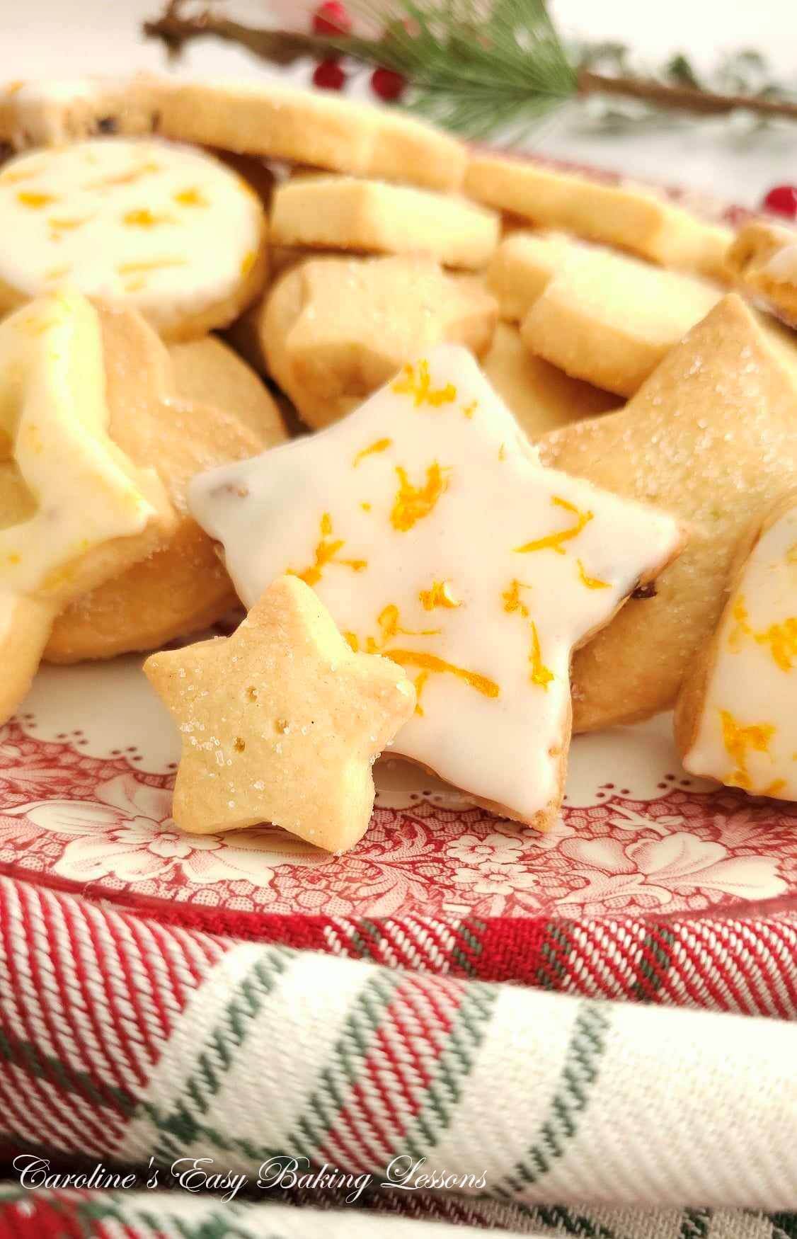 Extra extra close partial shot of various sizes and shapes of Scottish shortbread, with some star shaped and an orange glaze & zest on top, with tartin napkin.