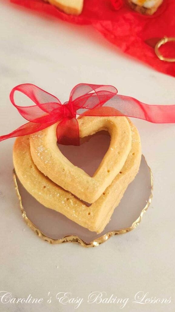 Close photo of a stack of 2 heart shape Scottish shortbread biscuits with heart insert cut out and tied with red ribbon.