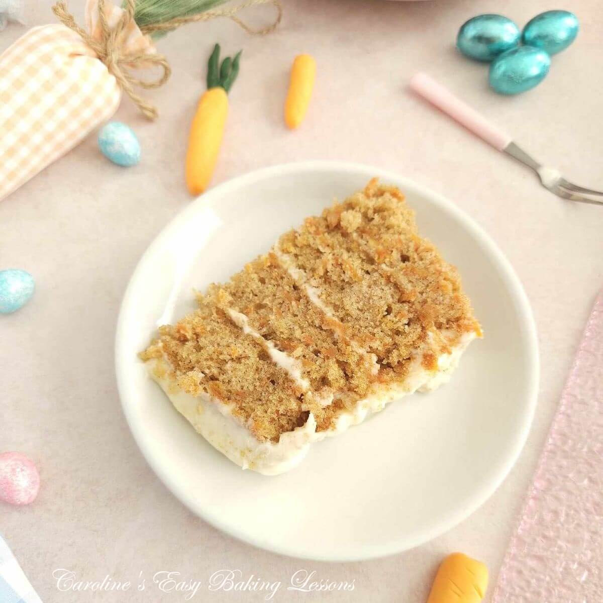 Shot of a whit eplate with 4 layer carrot cake slice,, soft pink pastel Spring decorations and mini eggs surrounding it.