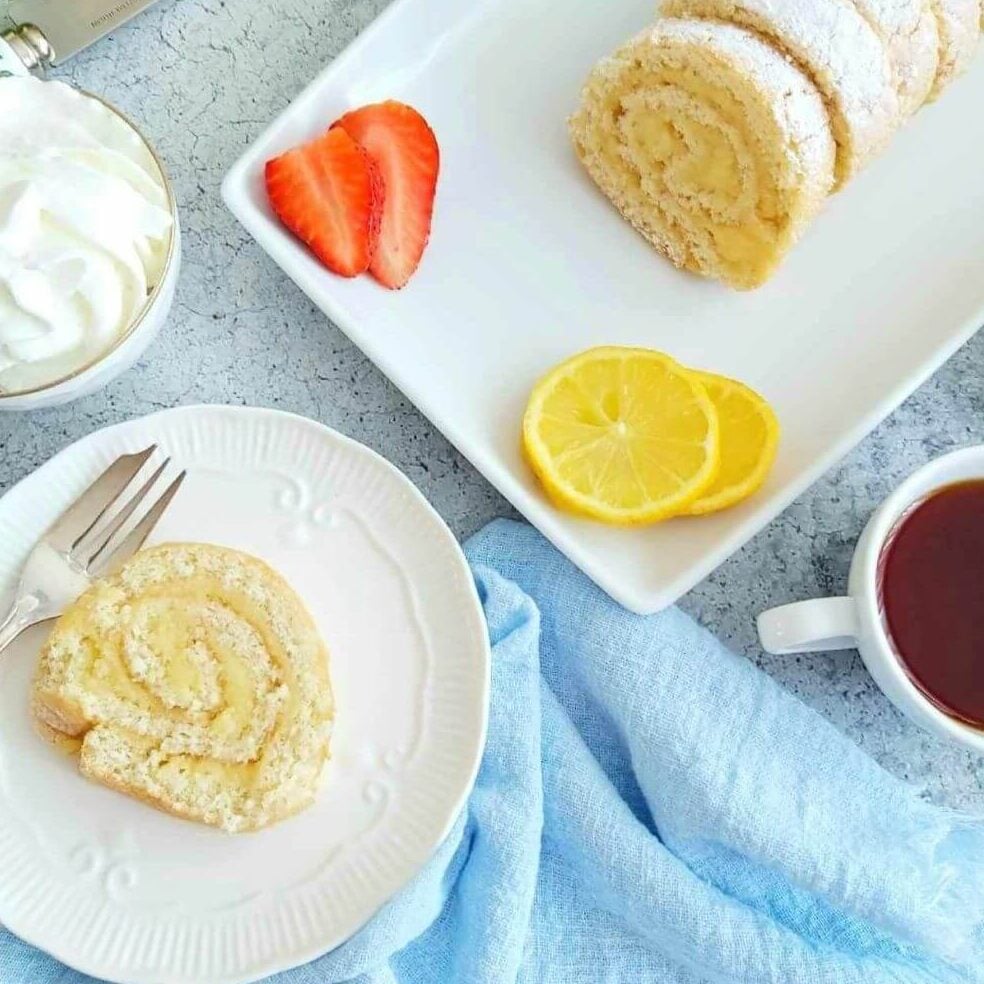Overhead photo of table with lemon curd filled Swiss roll on plater and slice served with coffee.