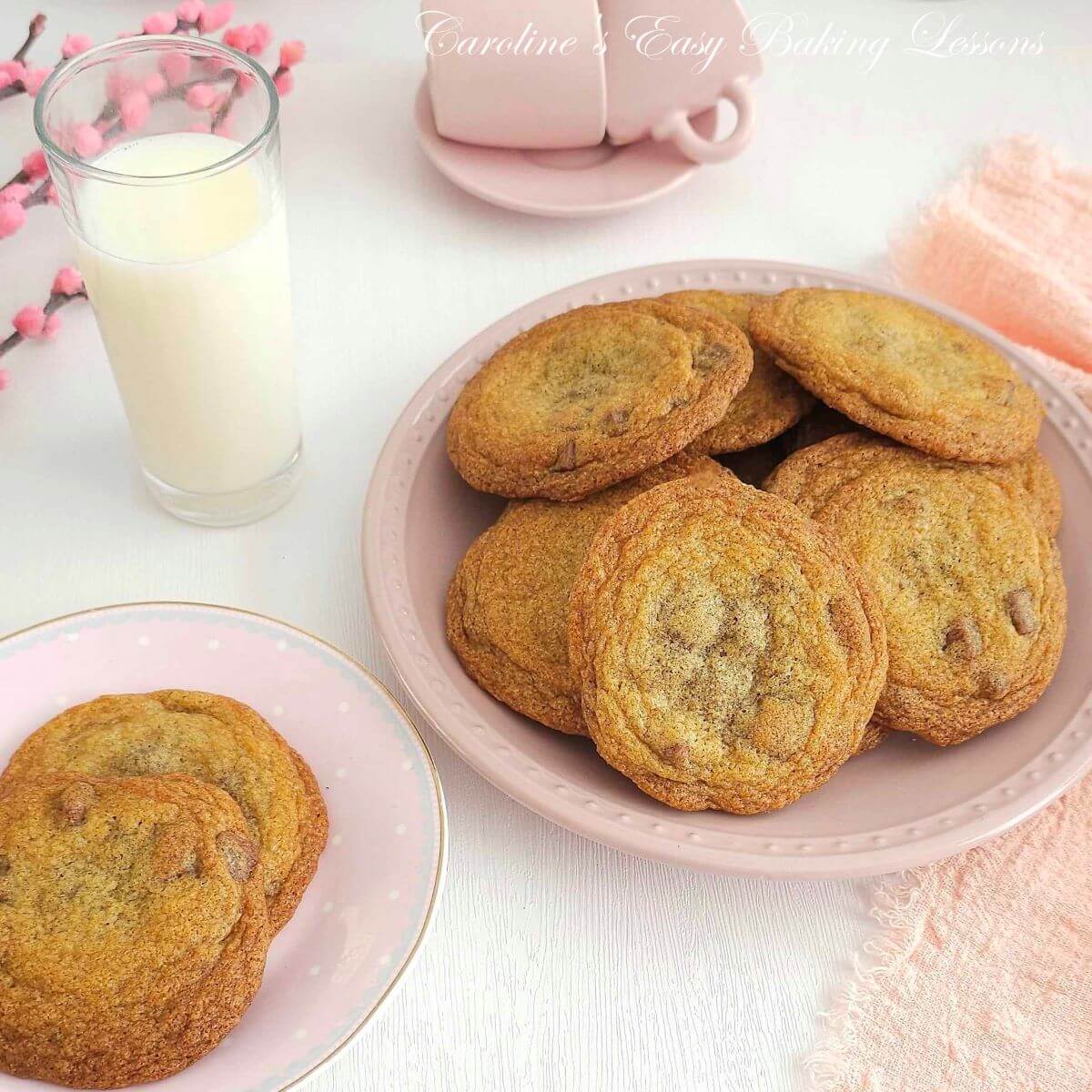 Photo of large soft chocolate chip cookies on a pink plate, 2 on a small plate and glass of milk to the background.