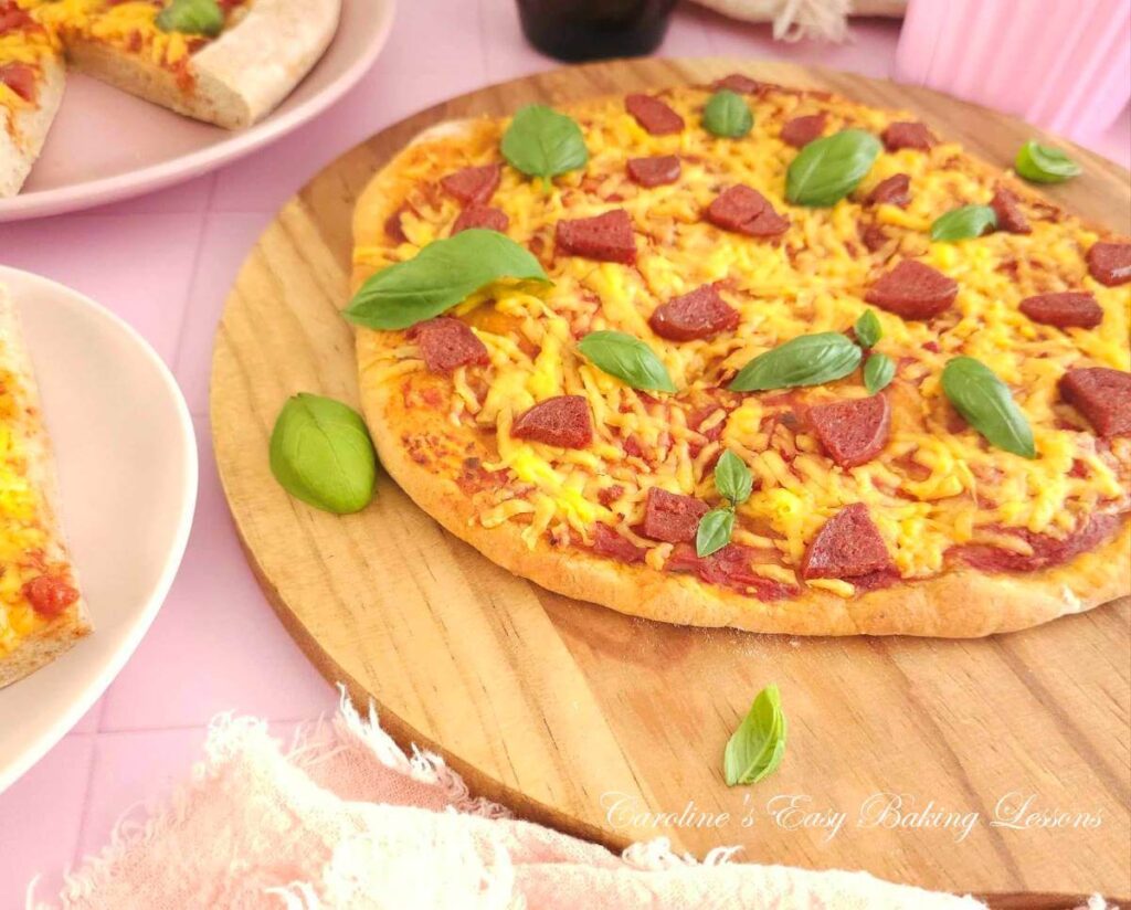 ANgled shot of a large cheese tomoato and meat pizza with basil leaves on a wooden round chopping board.