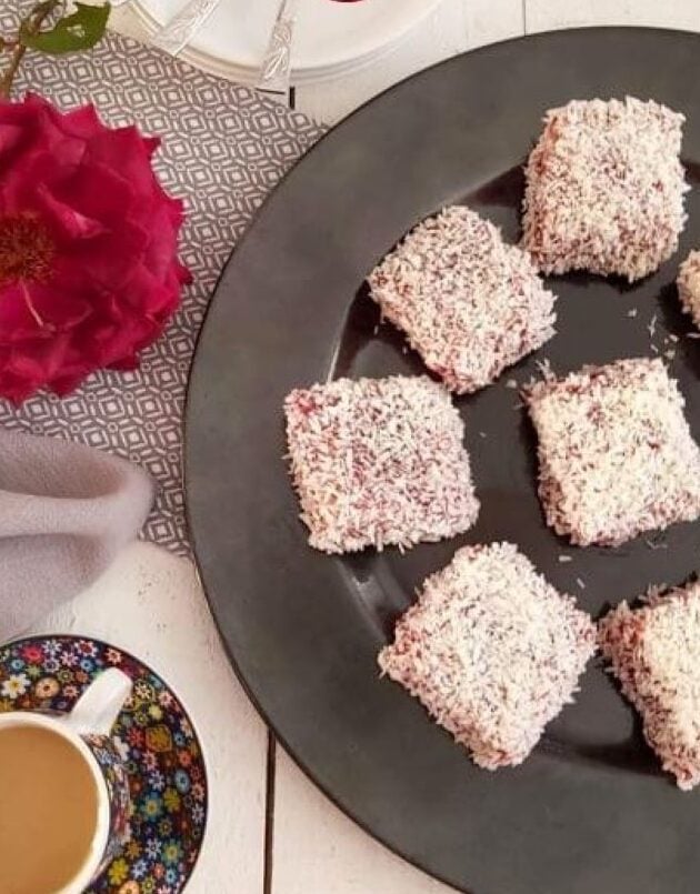 Overhead shot of a white table with jam and coconut covered cake squares on plate with tea, and title Lamingtons.