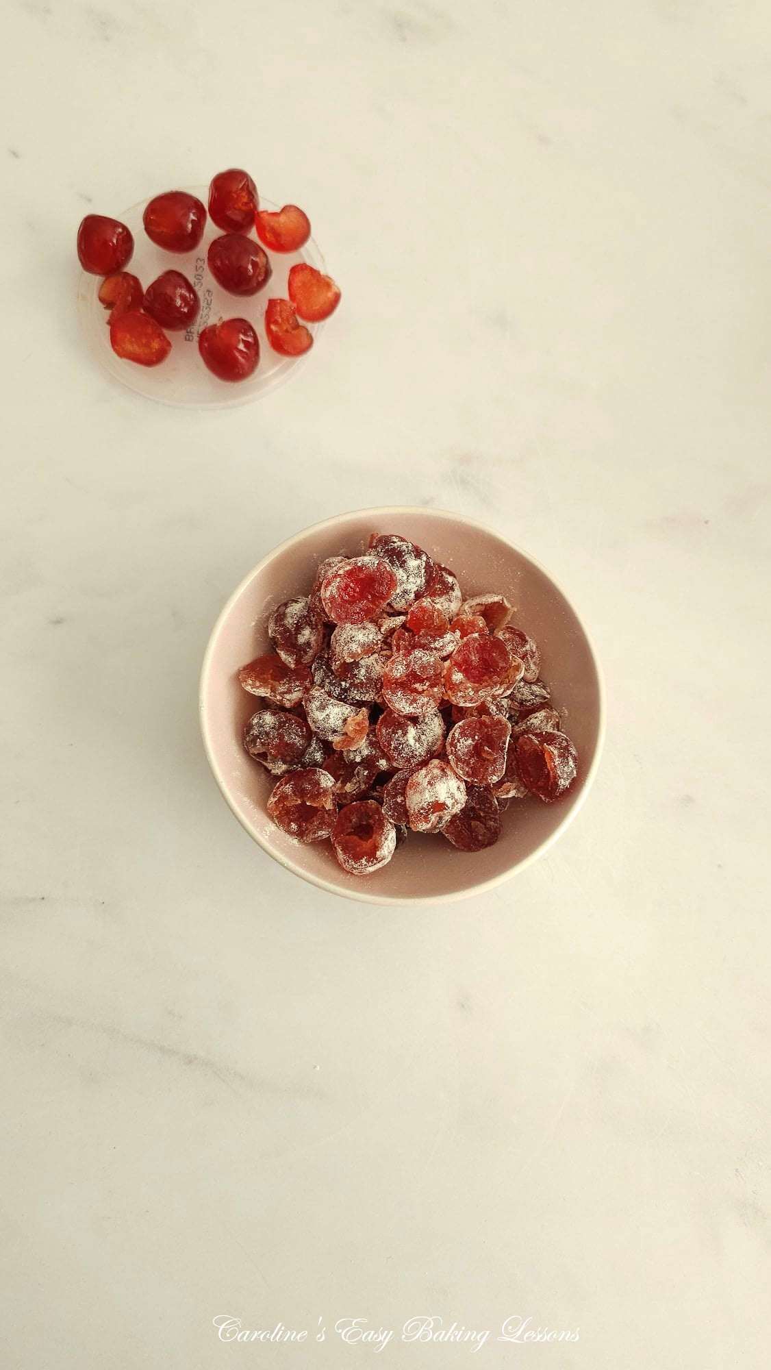 Overhead photo of bowl of glace cherries/candied cherries, coated in flour, and some whole as is at the background.