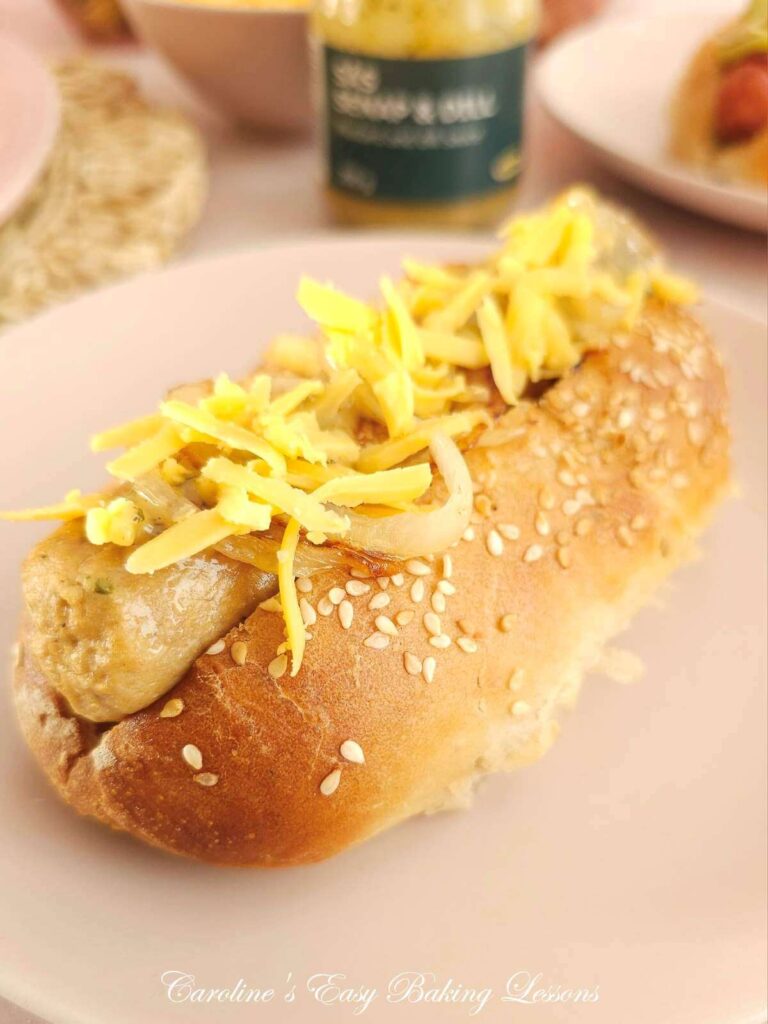 Extra close shot of a homemade hot dog bun, with Quorn sausage, mustard & onion, on a pink plate.