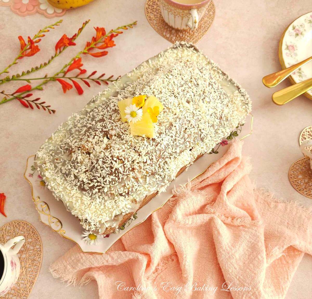 Photo of pink table with crokery and napkins, surrounding a coconut topped tropical banana bread loaf in the centre.