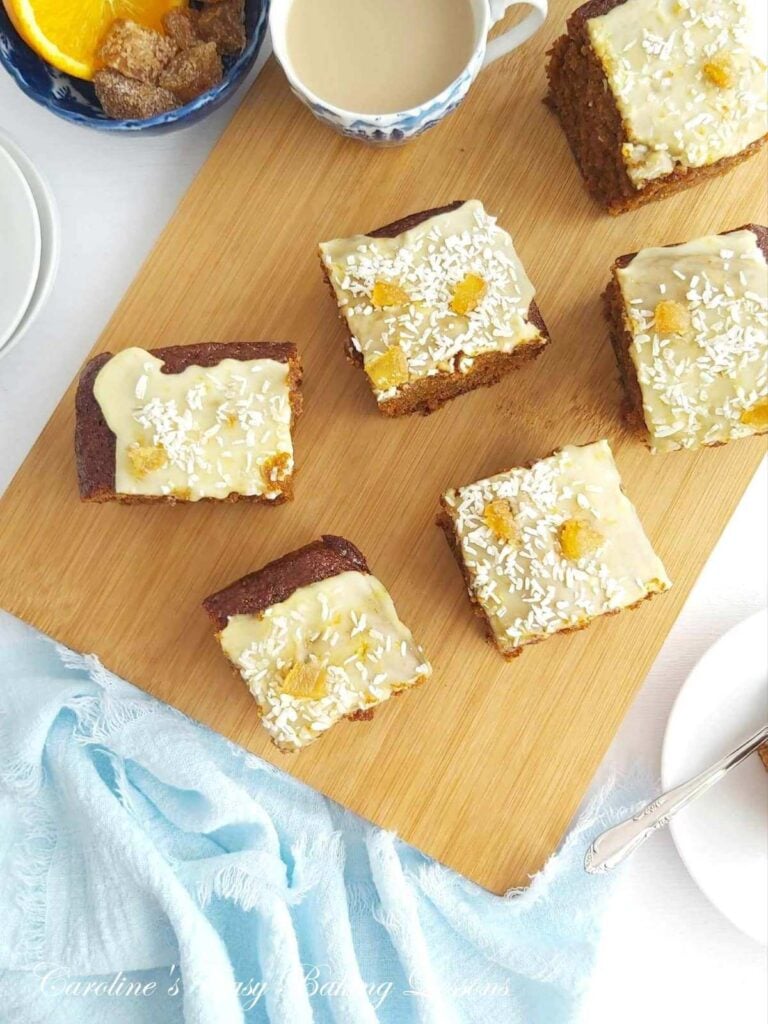 Overhead shot on a wooden chopping board several gingerbreade glazed cake squares.