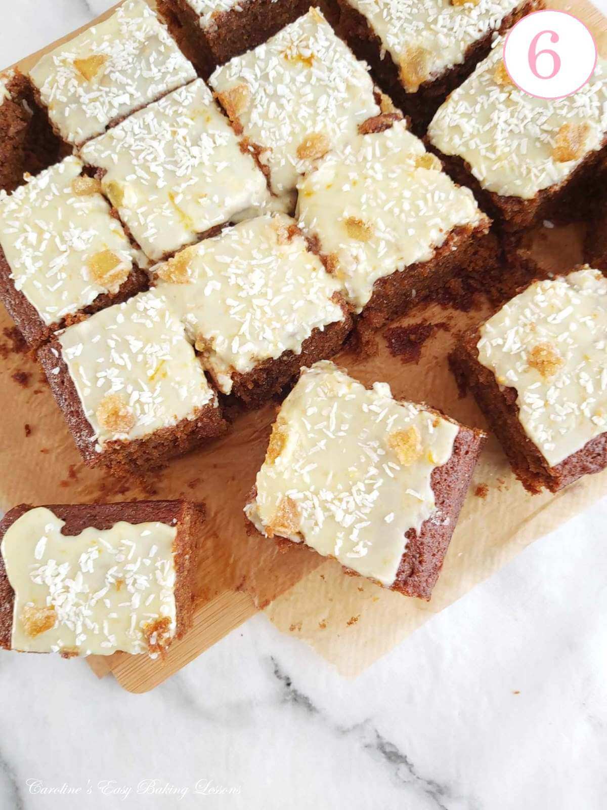 Close overhead shot of wooden chopping board with square gingerbreak cake (traybake) glazed and cut into 16 squares, with text 'photo 6'.