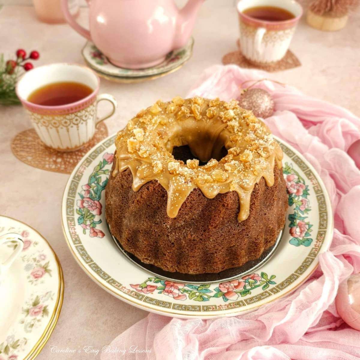 Close shot if a Christmas dining table with pink crokery and a golden butterscotch glazed gingerbread bundt cake in the centre.