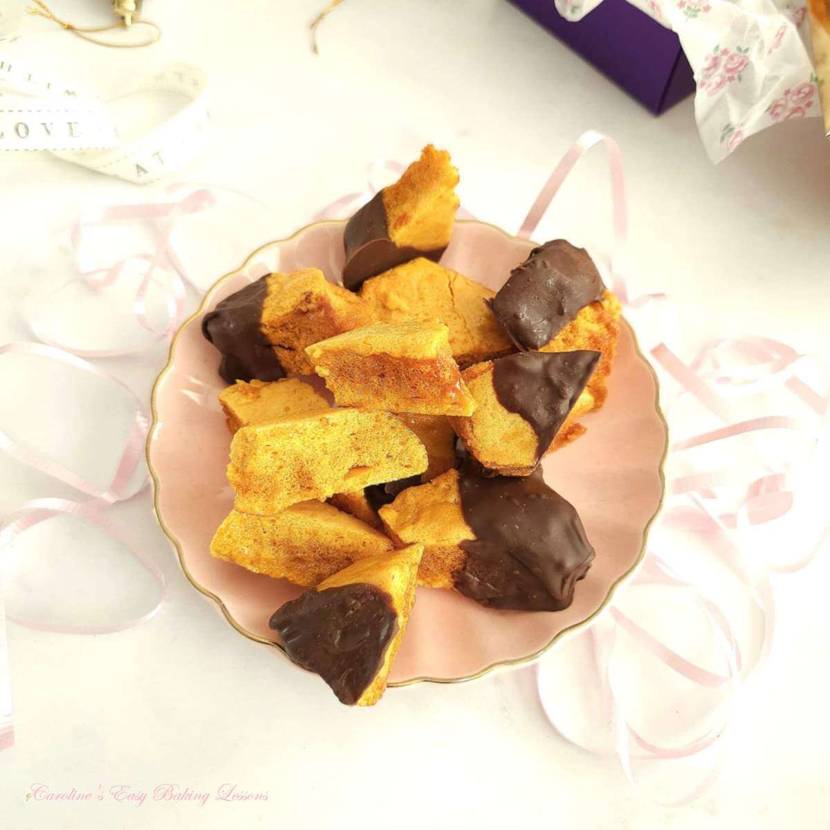 Overhead photo on white table top with pink plate of half chocolate coated honeycomb (sponge candy) pieces.
