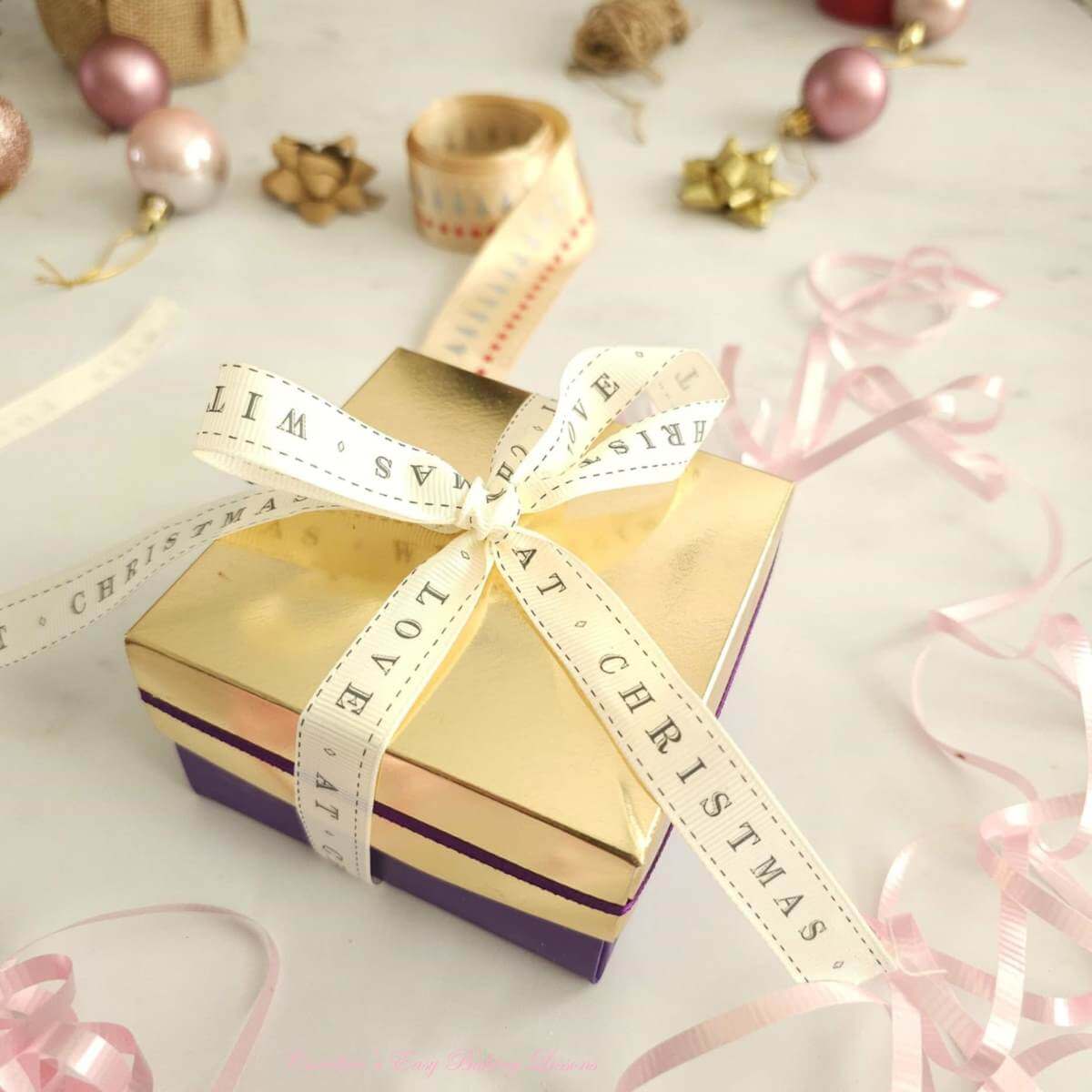 Small gift box with ribbon with 'Christmas' printed on it, baubbles and ribbon at the background.