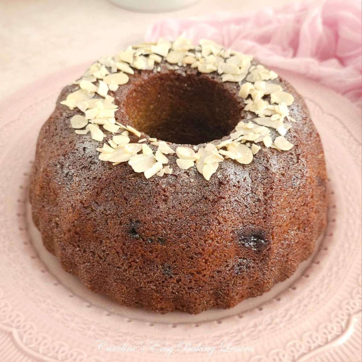 Close shot of a flaked alond topped, silver sprakle bundt cake, on pink plate.