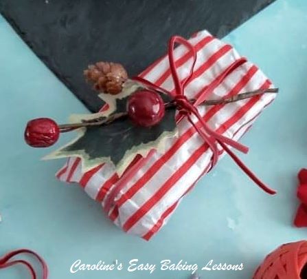 Close shot of red and white striped paper wrapped round Madeira cake slices, with ribbon and foliage.