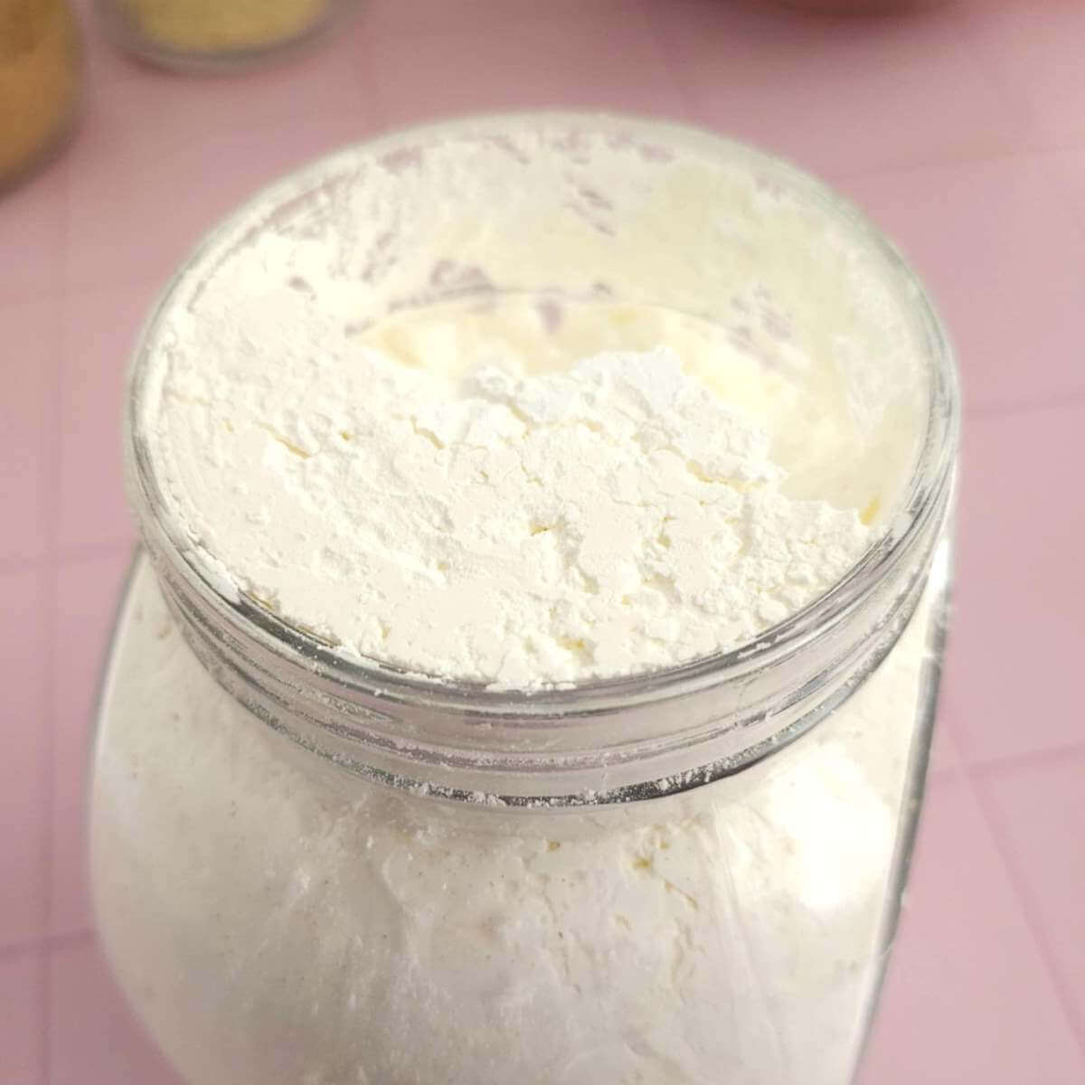 Extra close partial shot of a glass jar of cornflour (corn starch), with open lid.