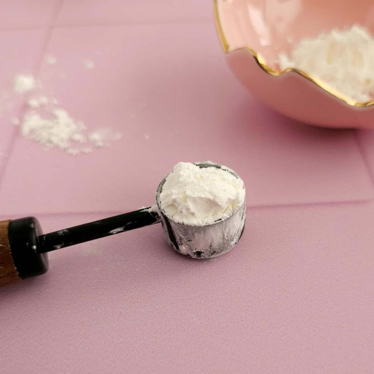 Extra close shot of a black measuring teaspoon, with heaped measure of cornflour/corn starch.